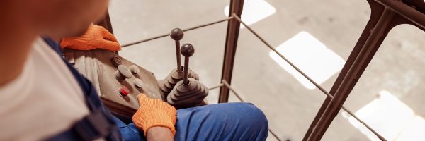 Close up of young man in work gloves sitting in operator cabin and pressing button