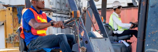 African American foreman or cargo container worker drive cargo car beside of his co-worker woman in workplace area. Industrial support system help employee performance concept.