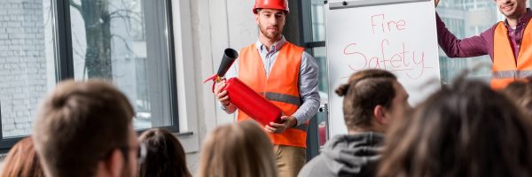 selective focus of handsome fireman in helmet holding extinguisher while standing near white board